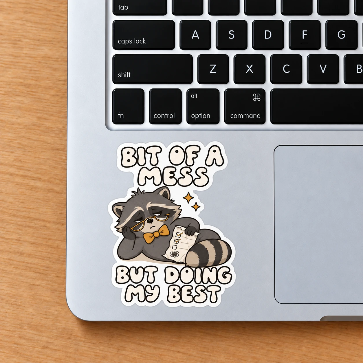 Bit of a Mess Sticker, Checklist Raccoon design shown on a laptop palm rest